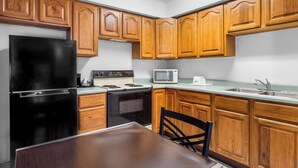 A kitchen with wooden cabinets, a black refrigerator, a stove, a microwave, and a sink.