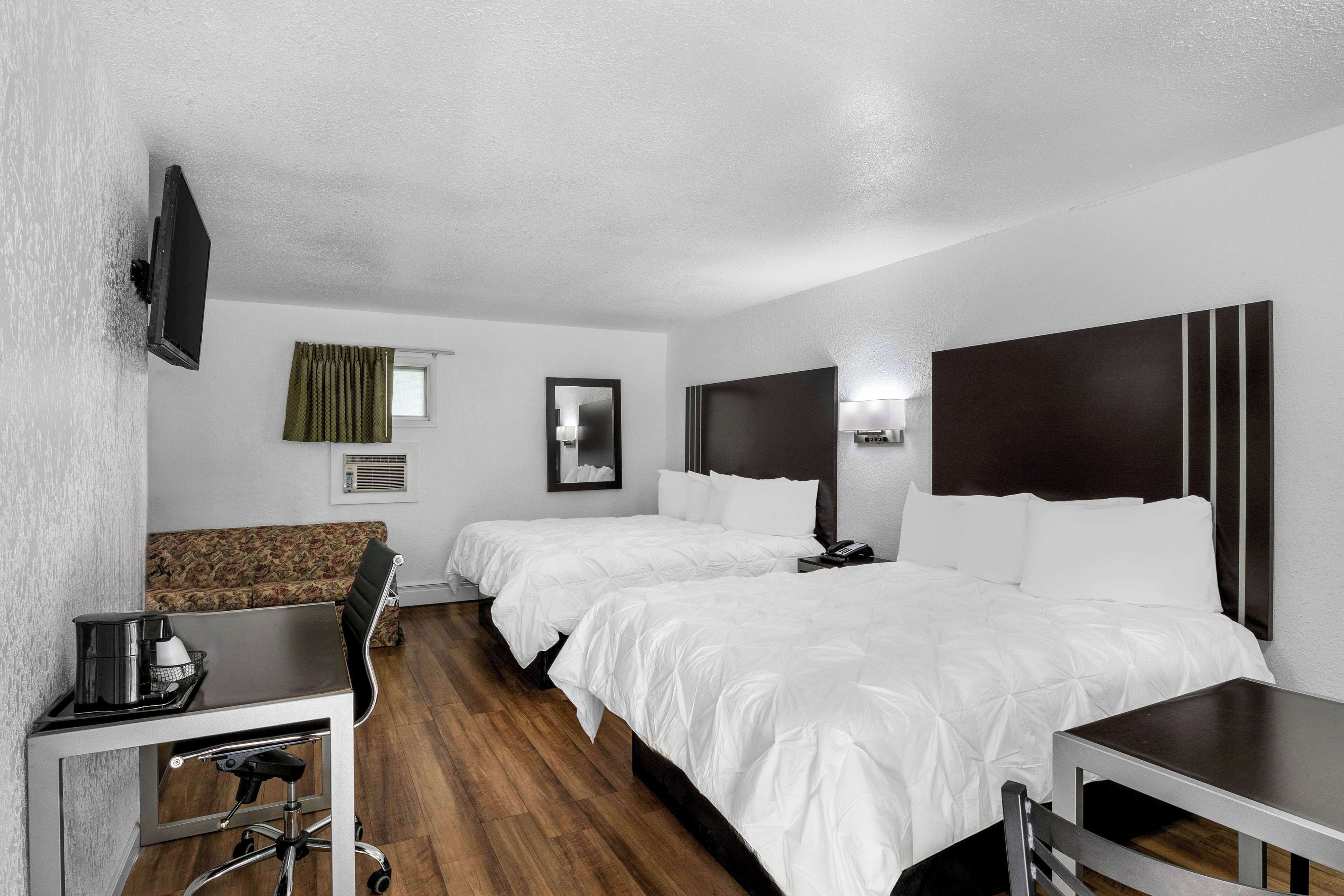 A hotel room with two beds, a desk, a chair, a TV, and a window with curtains.