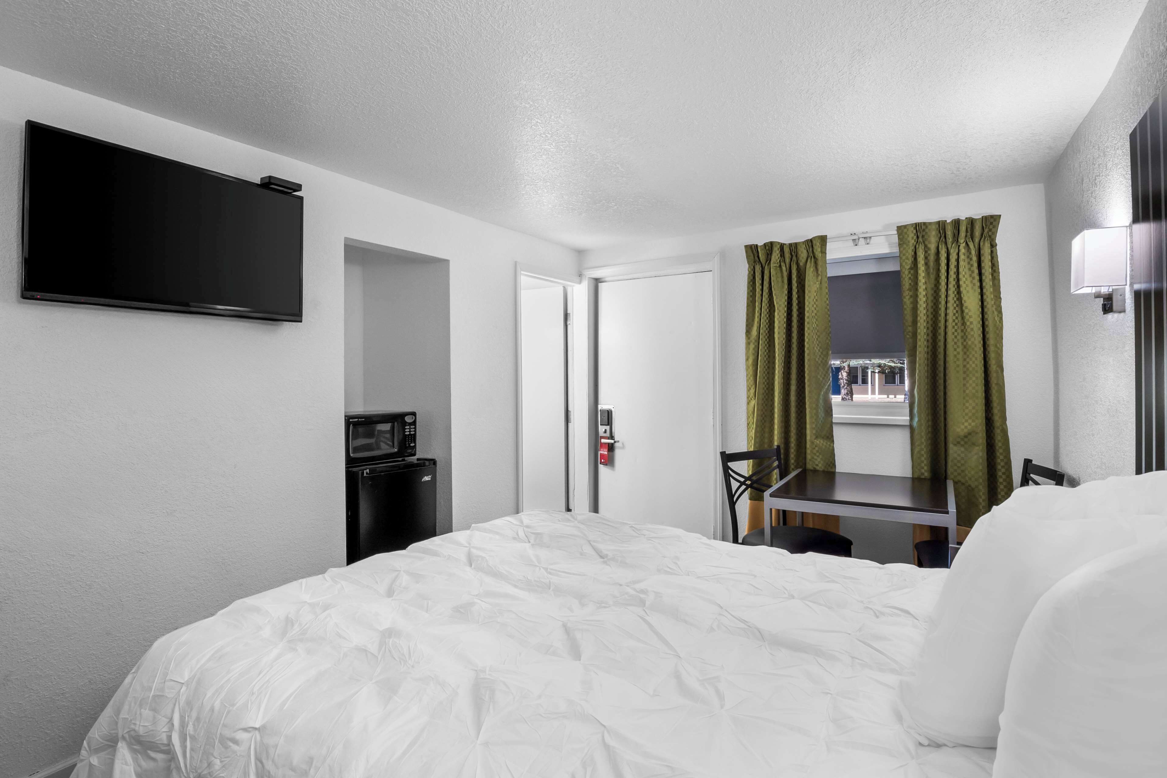 Quarto de hotel com cama, escrivaninha, TV de tela plana, micro-ondas e janela com cortinas.