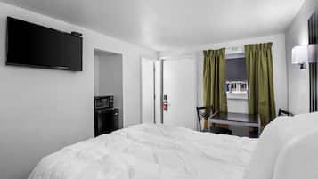 A hotel room with a bed, a desk, a flat-screen TV, a microwave, and a window with curtains.