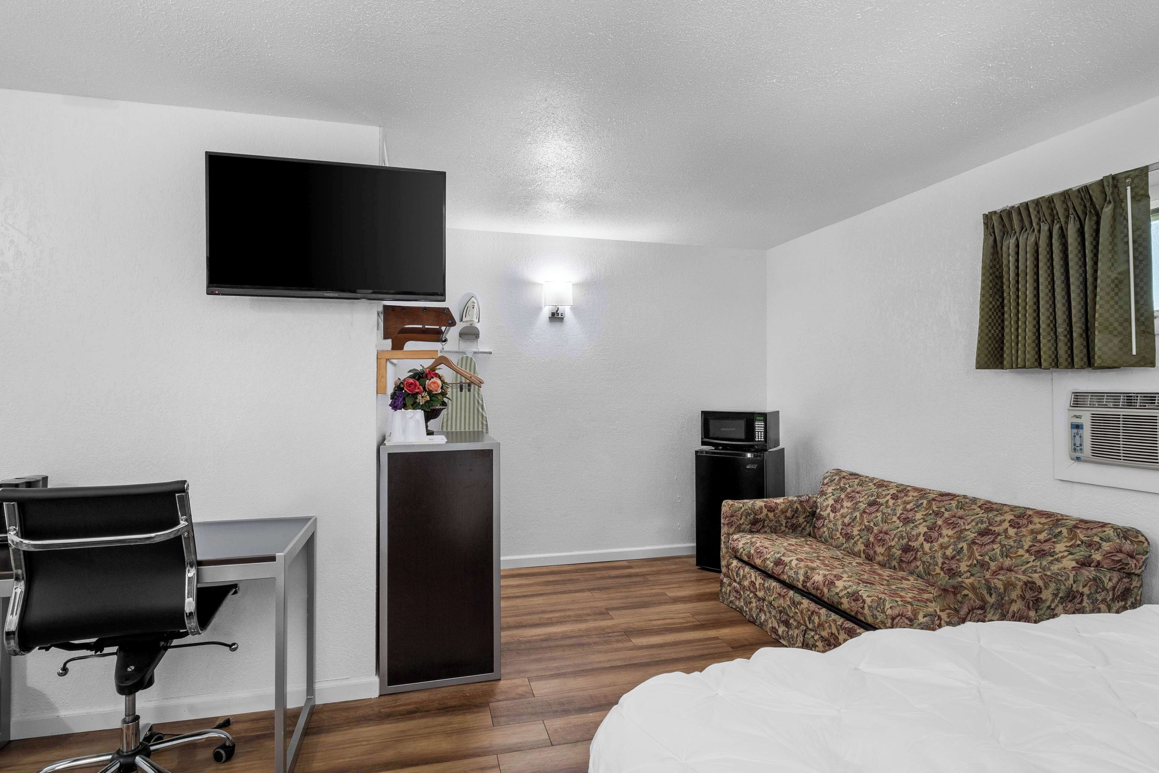 Une chambre d’hôtel comprenant un lit, un bureau avec une chaise, une télévision, un petit meuble, un four à micro-ondes et un canapé à motifs floraux.
