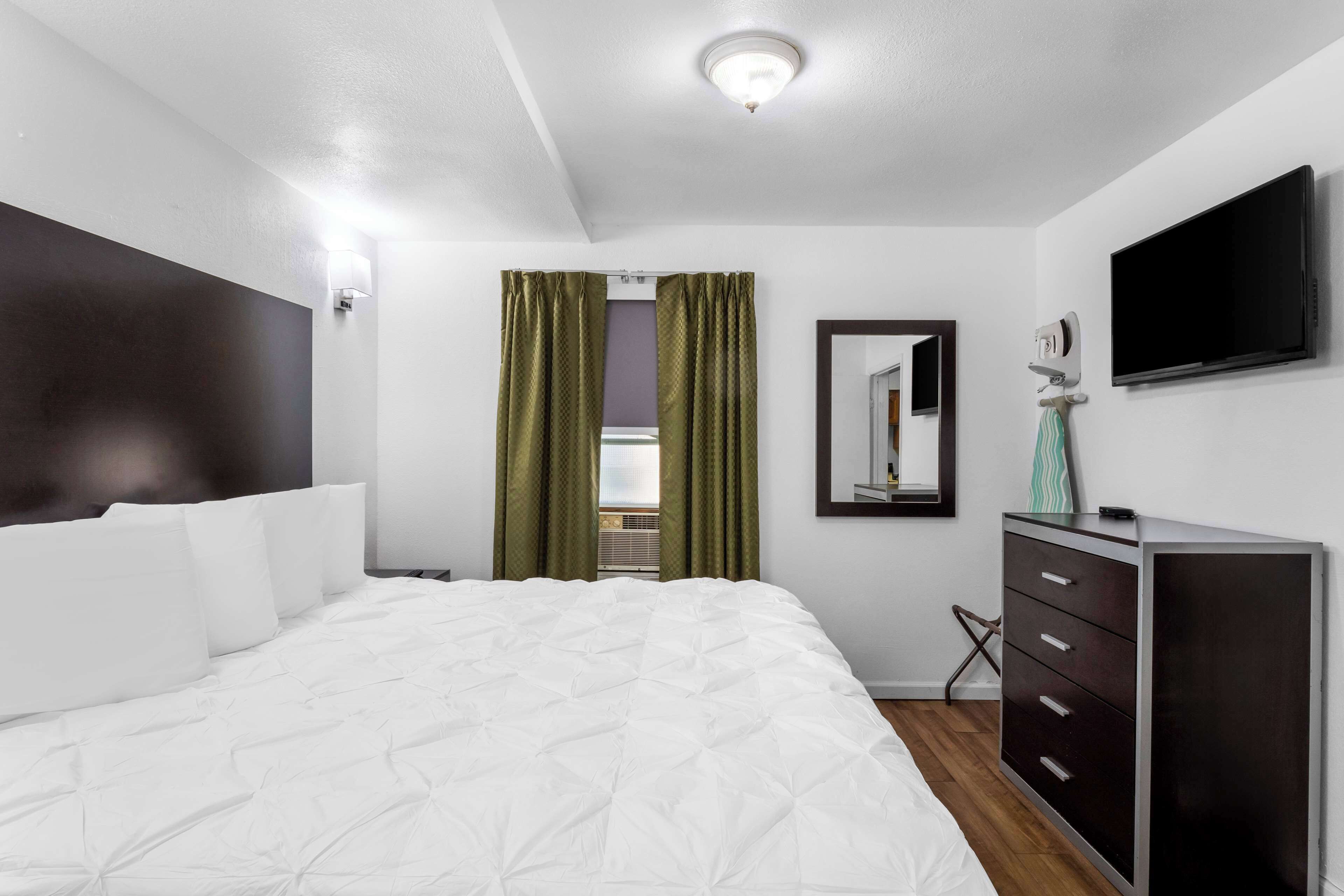 A modern hotel room with a large bed, a dresser, a television, and a mirror.
