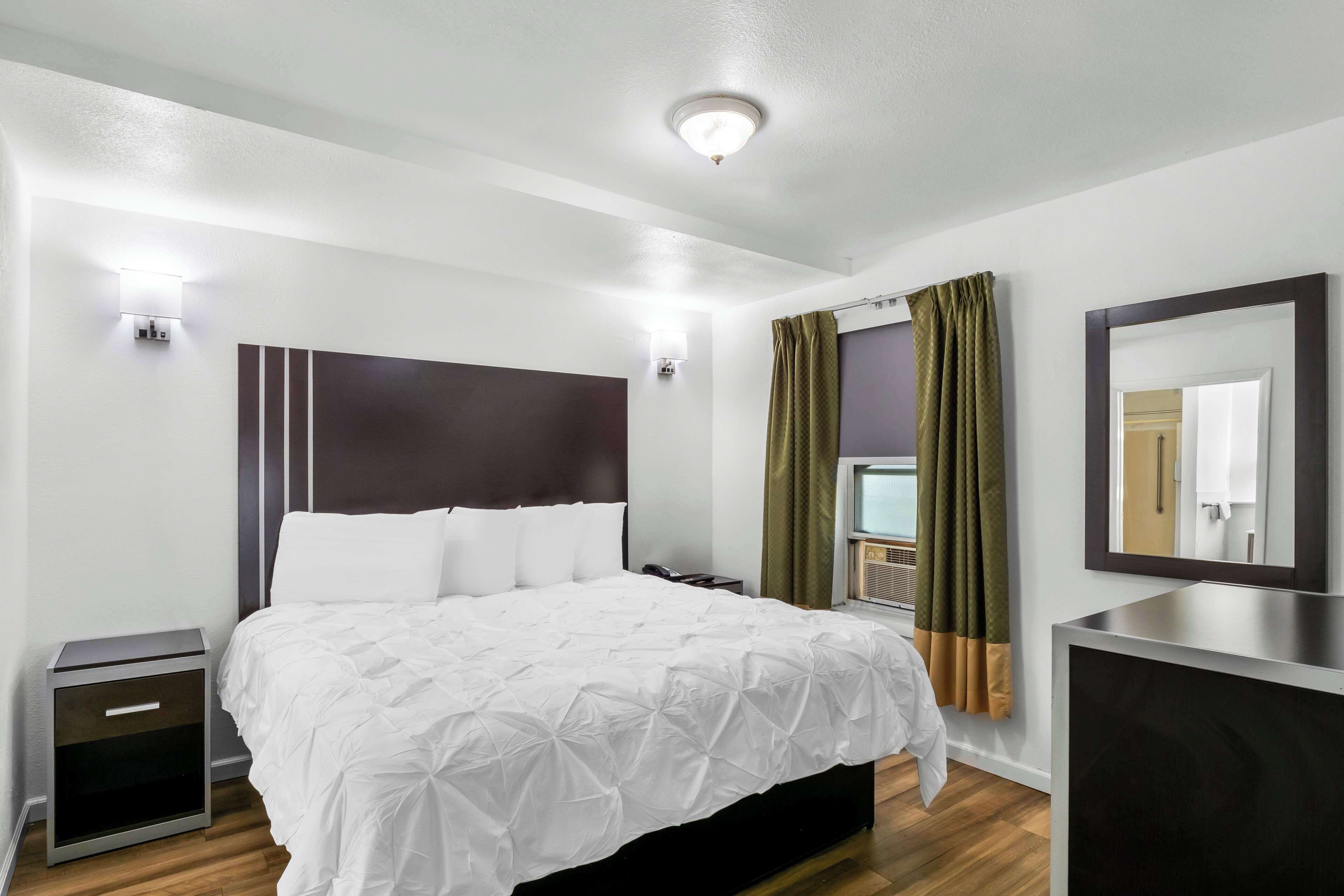 Una habitación de hotel moderna con una cama grande, mesitas de noche, un espejo y una ventana con cortinas.