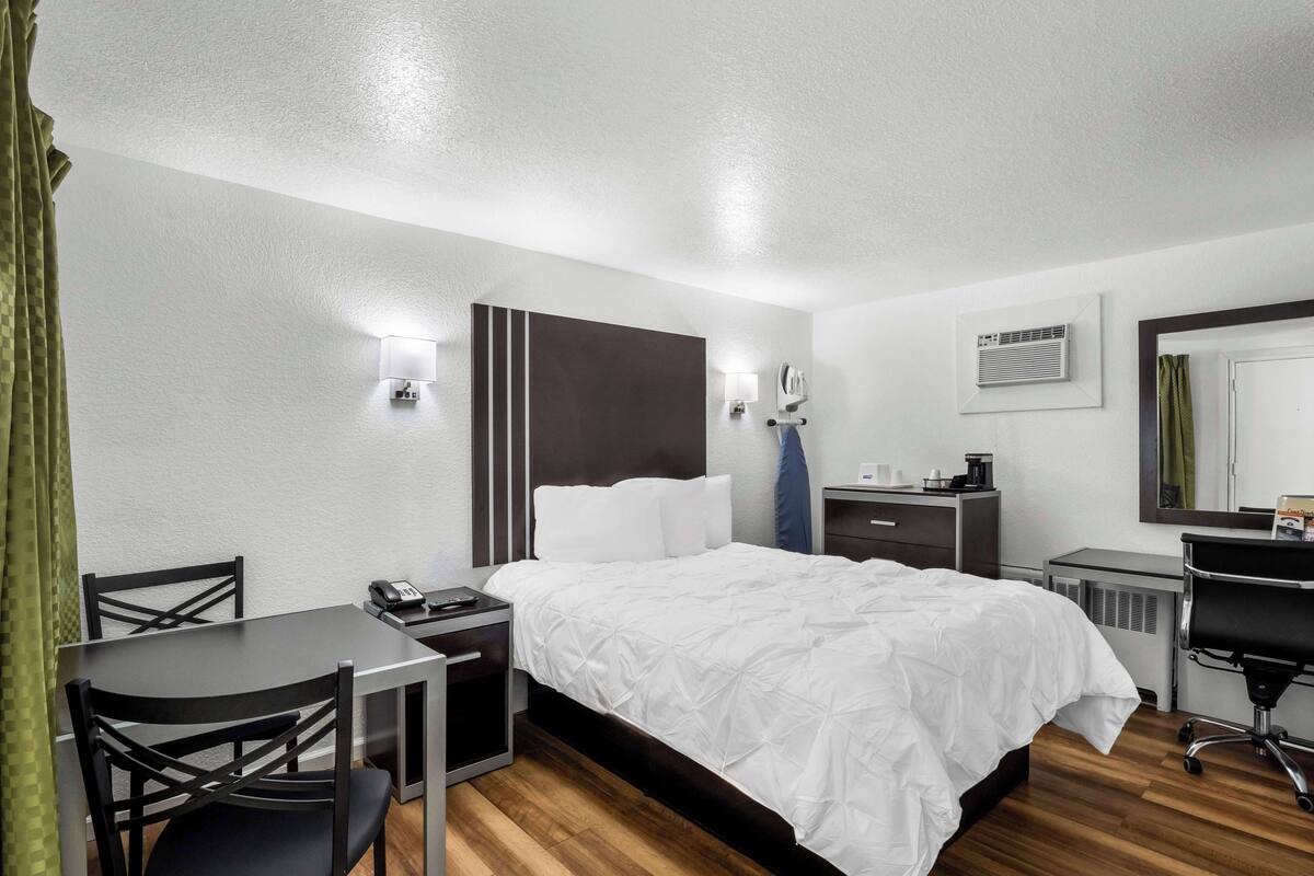 A hotel room with a bed, bedside table, chair, desk, and a mirror.