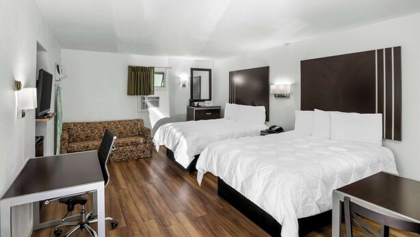 A hotel room with two beds, a desk, a chair, a TV, and a sofa.