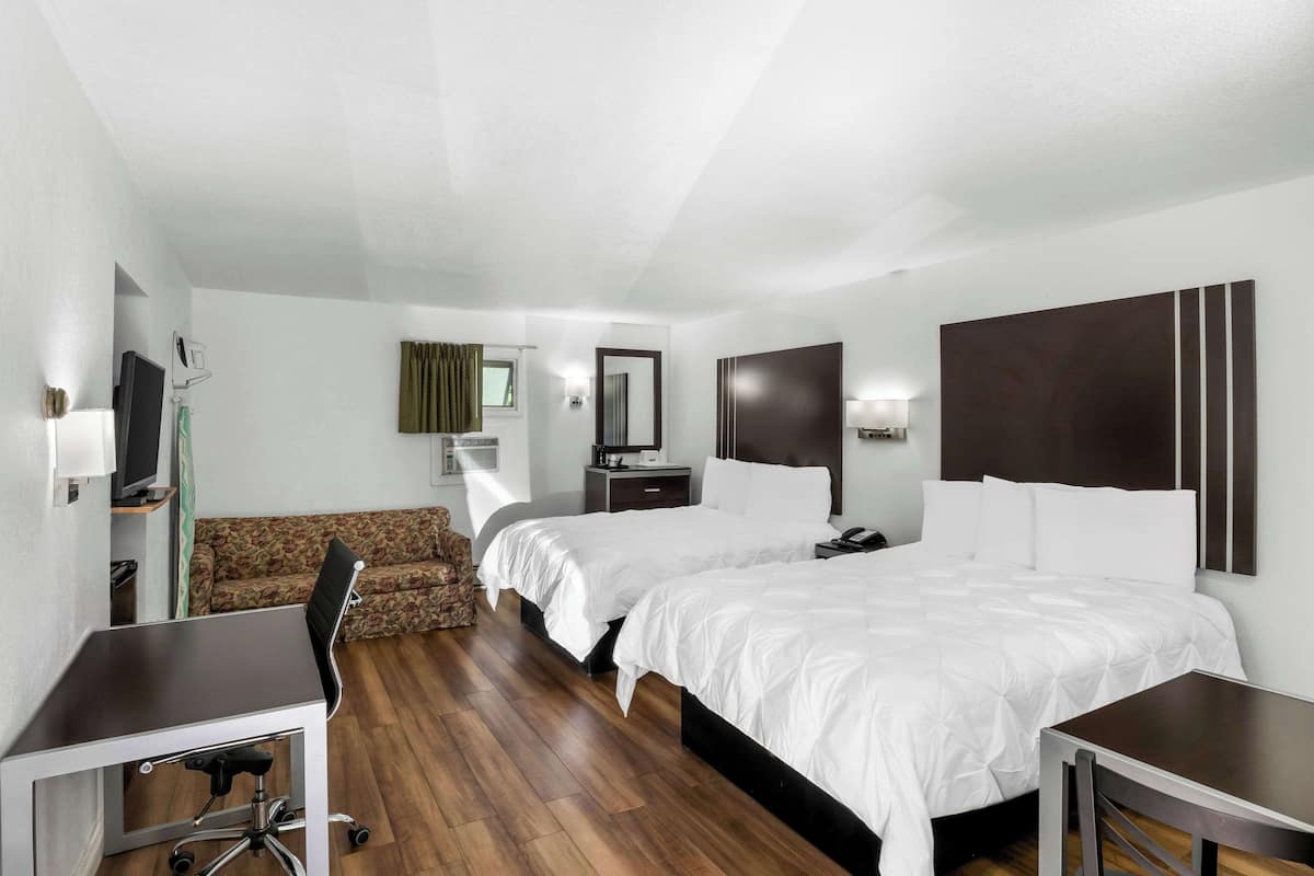 A hotel room with two beds, a desk, a chair, a TV, and a sofa.