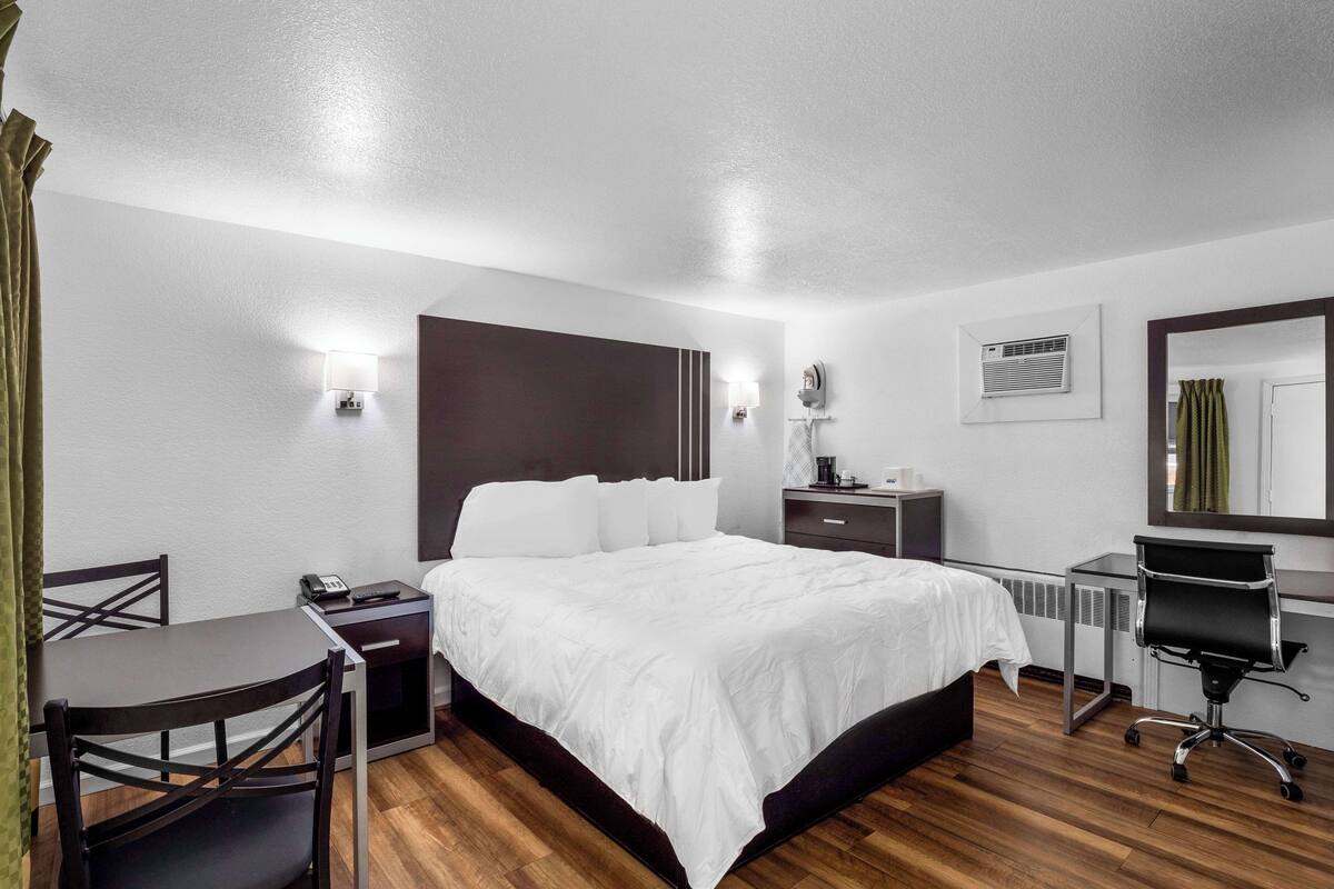 A hotel room with a large bed, a desk with a chair, a desk lamp, a telephone, and a mirror.