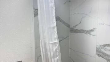 Un baño con cortina de ducha, inodoro y paredes con diseño de mármol.