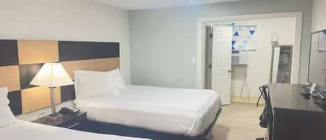 A hotel room with two beds, a desk, a lamp, and a wardrobe.