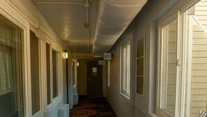 A hotel corridor with patterned carpet, large windows, and an exit sign. - Bourne Bridge Inn  (Buzzards Bay)