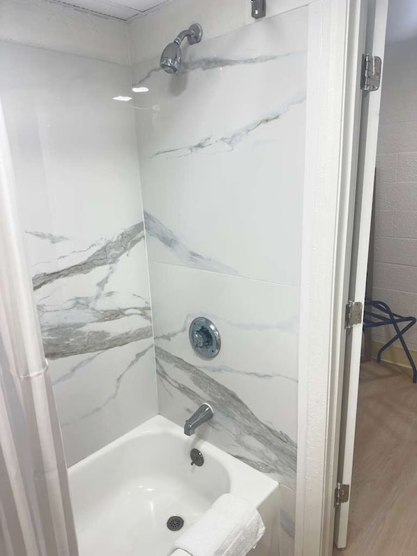 A bathroom with a shower, a sink, and a marble wall.