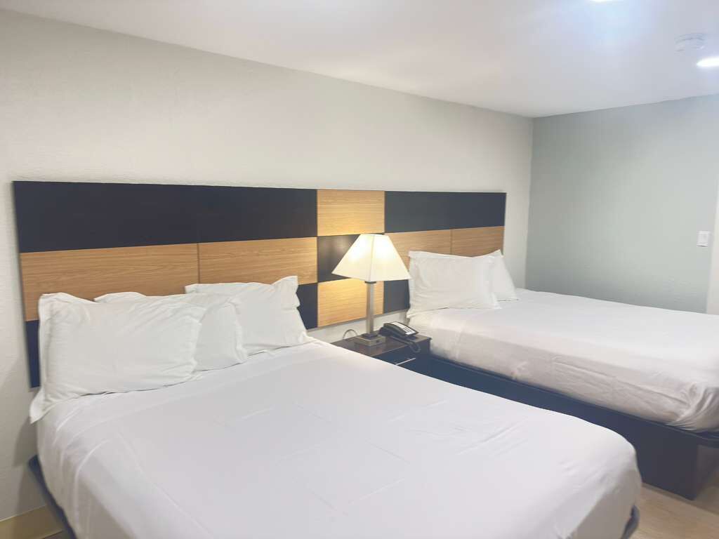 A hotel room with two beds, a nightstand with a lamp, and a modern headboard.