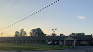 A motel with multiple rooms, a parking lot, and a small building with a covered area. - Slumber Inn Of Harrisonville (Harrisonville)