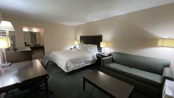 Habitación de hotel con cama, sofá, escritorio y una silla. Hay dos mesitas de noche con lámparas y un espejo sobre la cama.