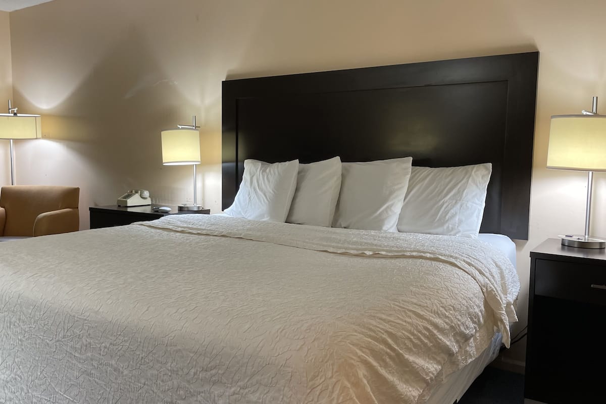 A hotel room with a large bed, two bedside tables, a chair, and a window with curtains.