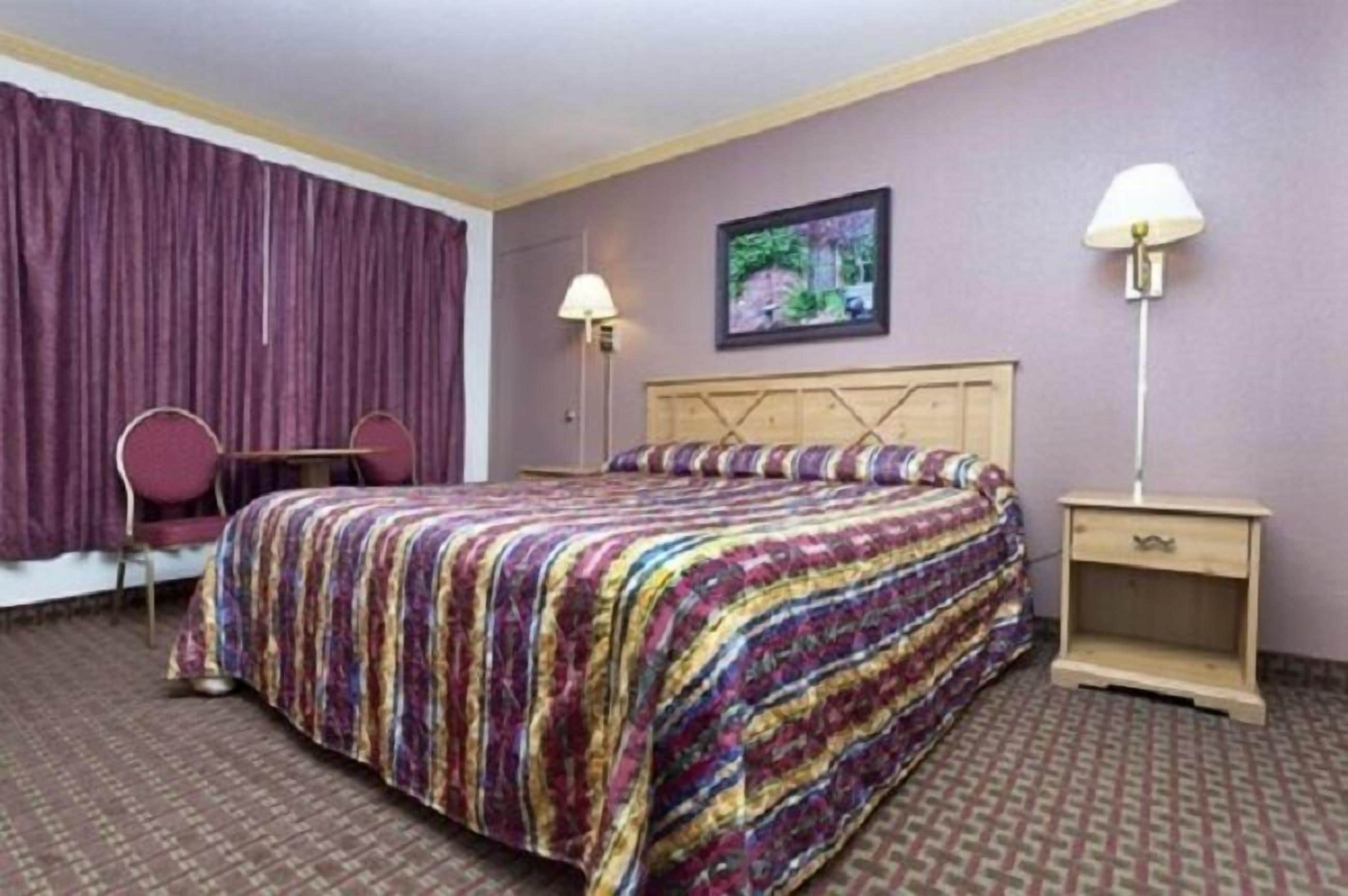 Habitación de hotel con una cama, dos lámparas de noche, una silla y un cuadro en la pared.