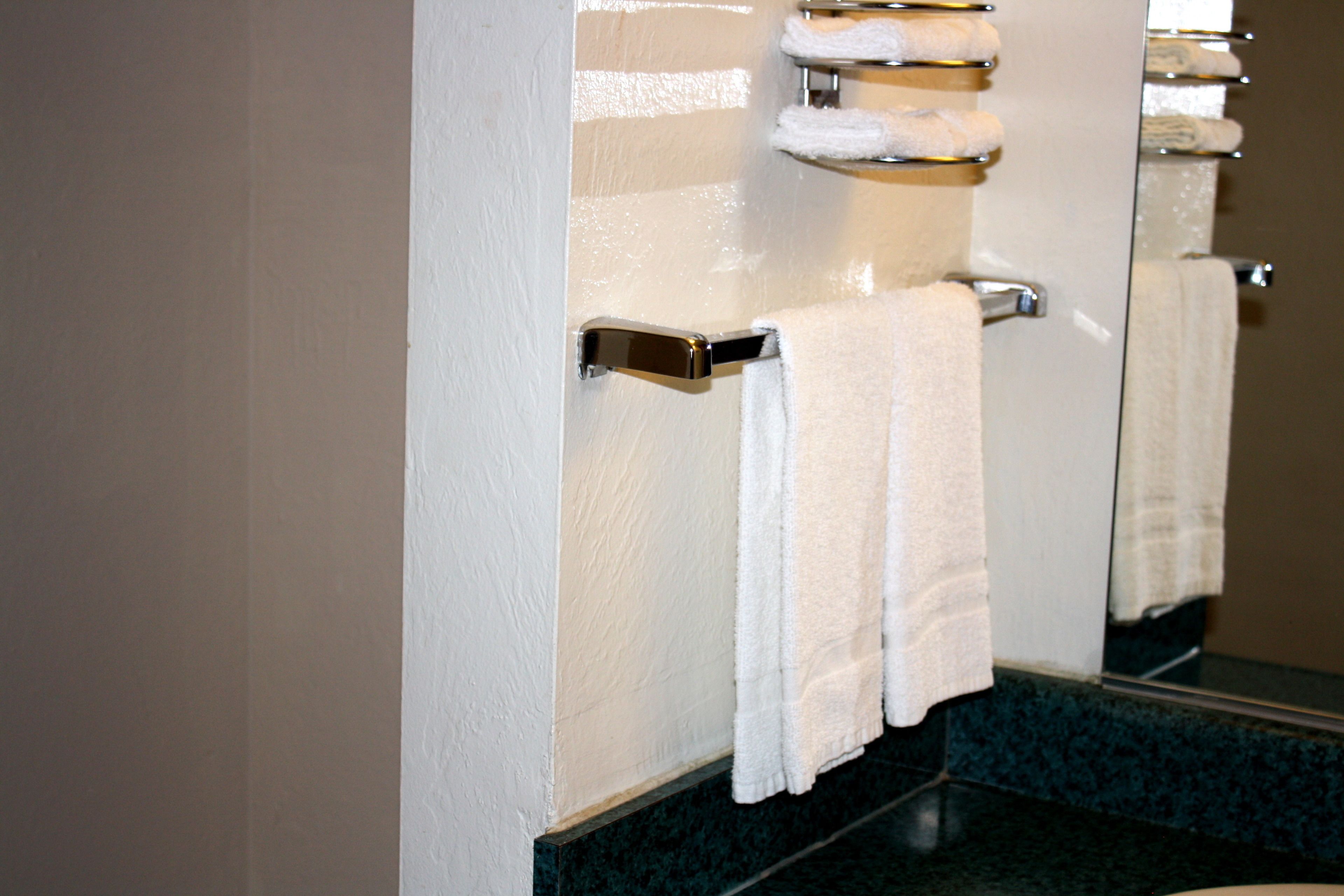 Un baño con pared blanca, un espejo y un perchero con una toalla blanca.