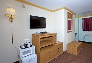 Habitación de hotel con televisión de pantalla plana, un escritorio de madera, microondas, cafetera y un pequeño armario de madera.