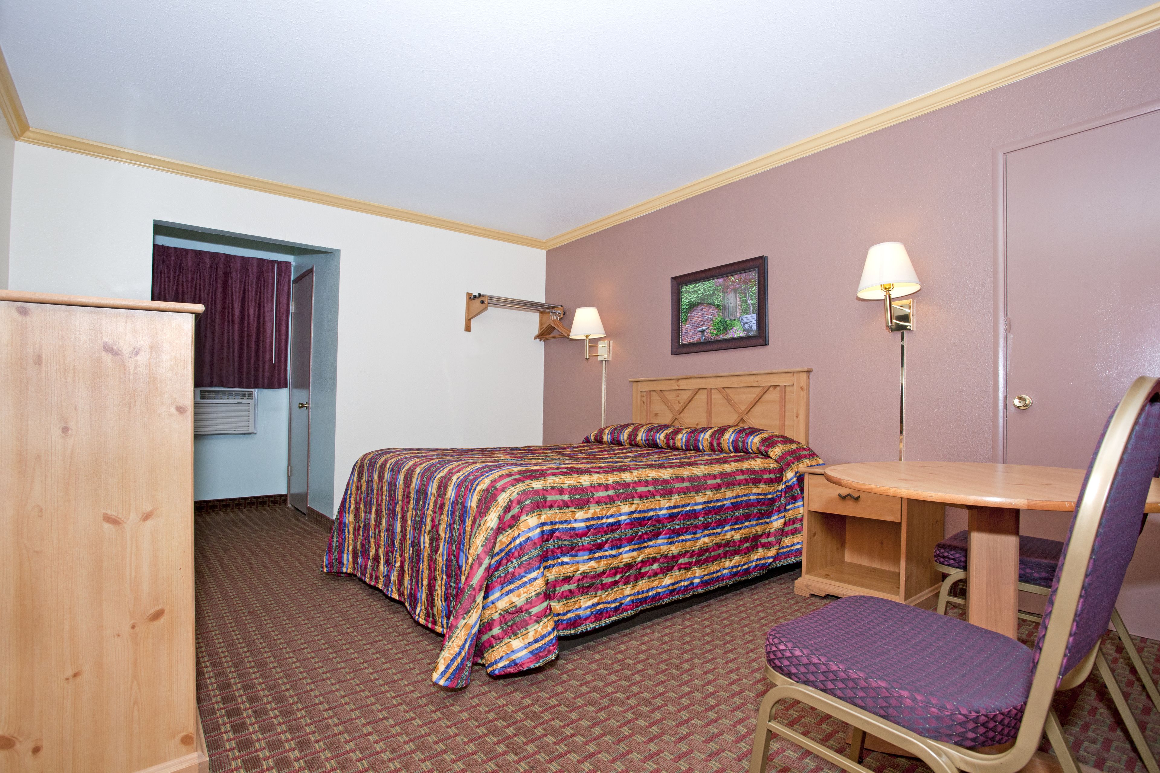 A hotel room with a bed, a desk, a chair, and a wardrobe.