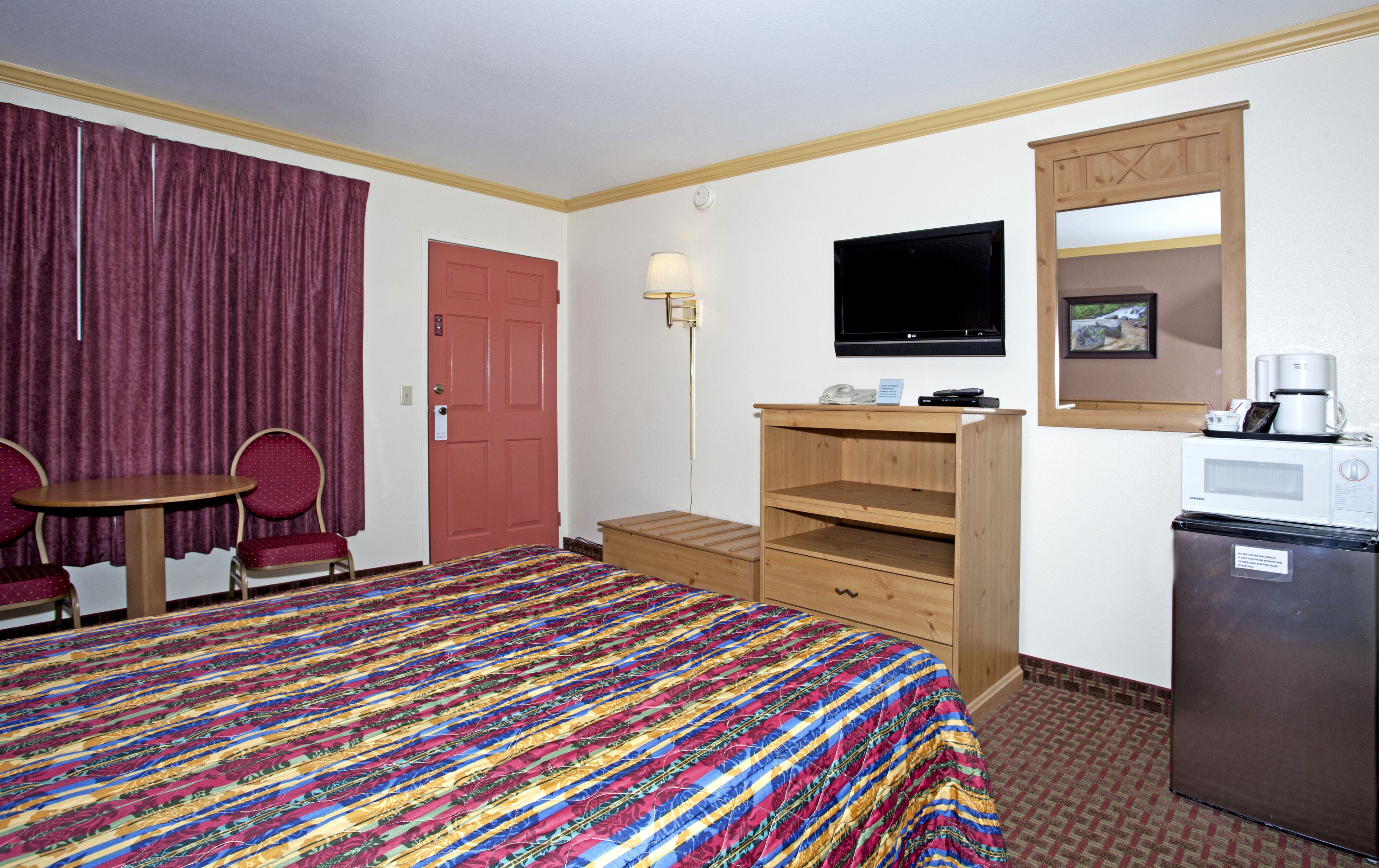 A hotel room with a bed, a desk, a chair, a television, a microwave, and a refrigerator.