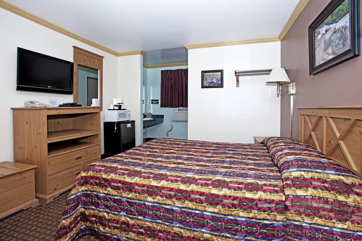 A hotel room with a large bed, wooden furniture, a flat-screen TV, a desk, and a bathroom visible through an open door.