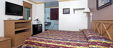 A hotel room with a large bed, wooden furniture, a flat-screen TV, a desk, and a bathroom visible through an open door.