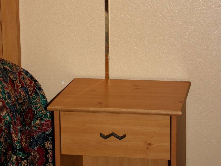 A wooden nightstand with a lamp, a drawer, and a patterned bedspread.