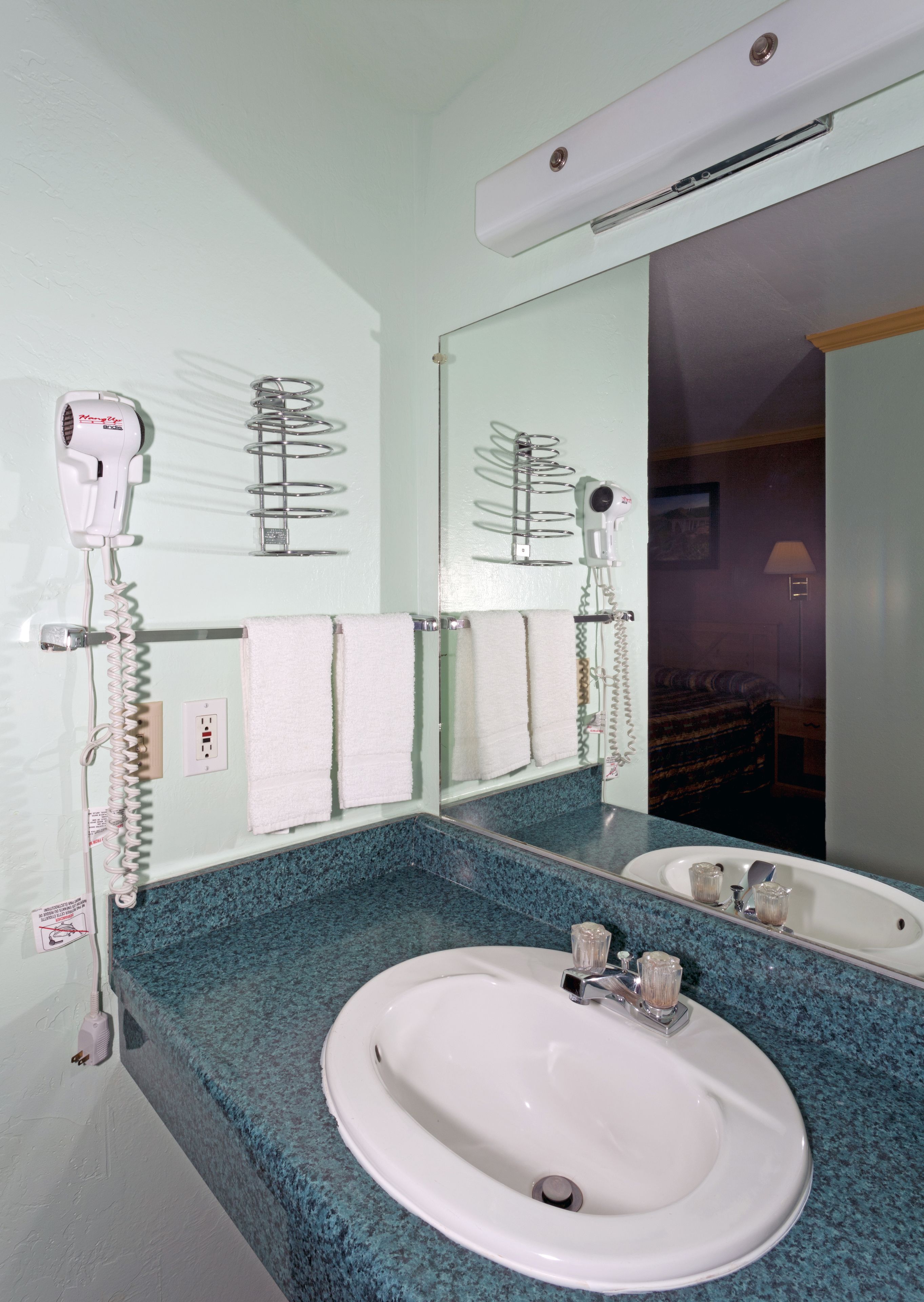 Un baño con un lavamanos blanco, un espejo y dos secadores de pelo montados en la pared.