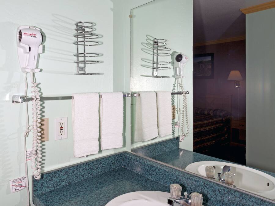 A bathroom with a white sink, a mirror, and two hair dryers mounted on the wall.