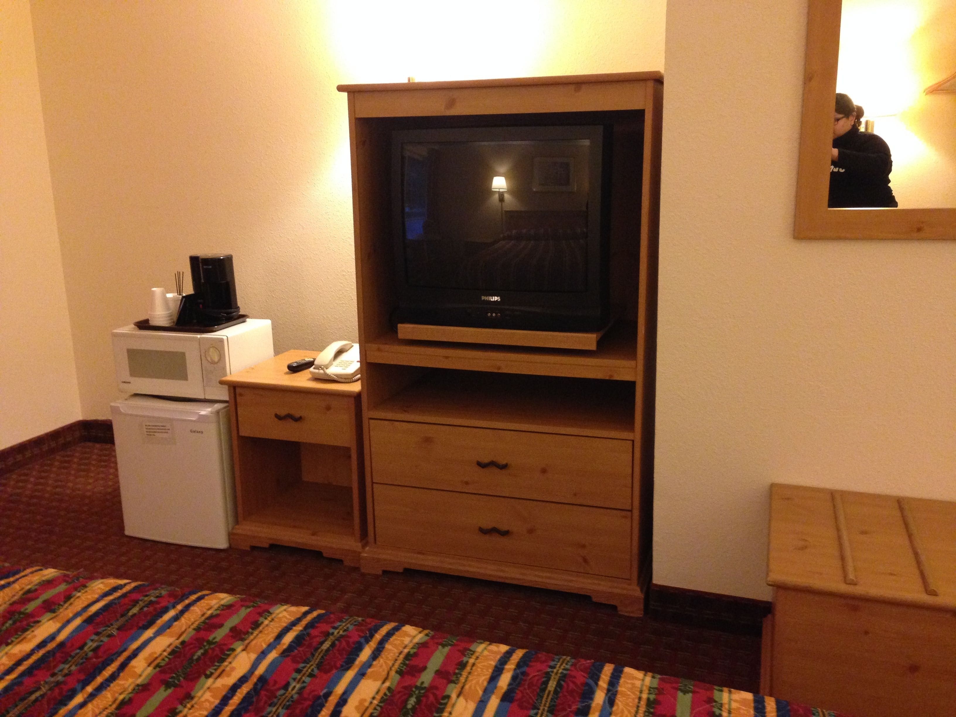 Habitació d'hotel amb televisió, microones, nevera, taula de nit amb telèfon i llit amb manta de ratlles.