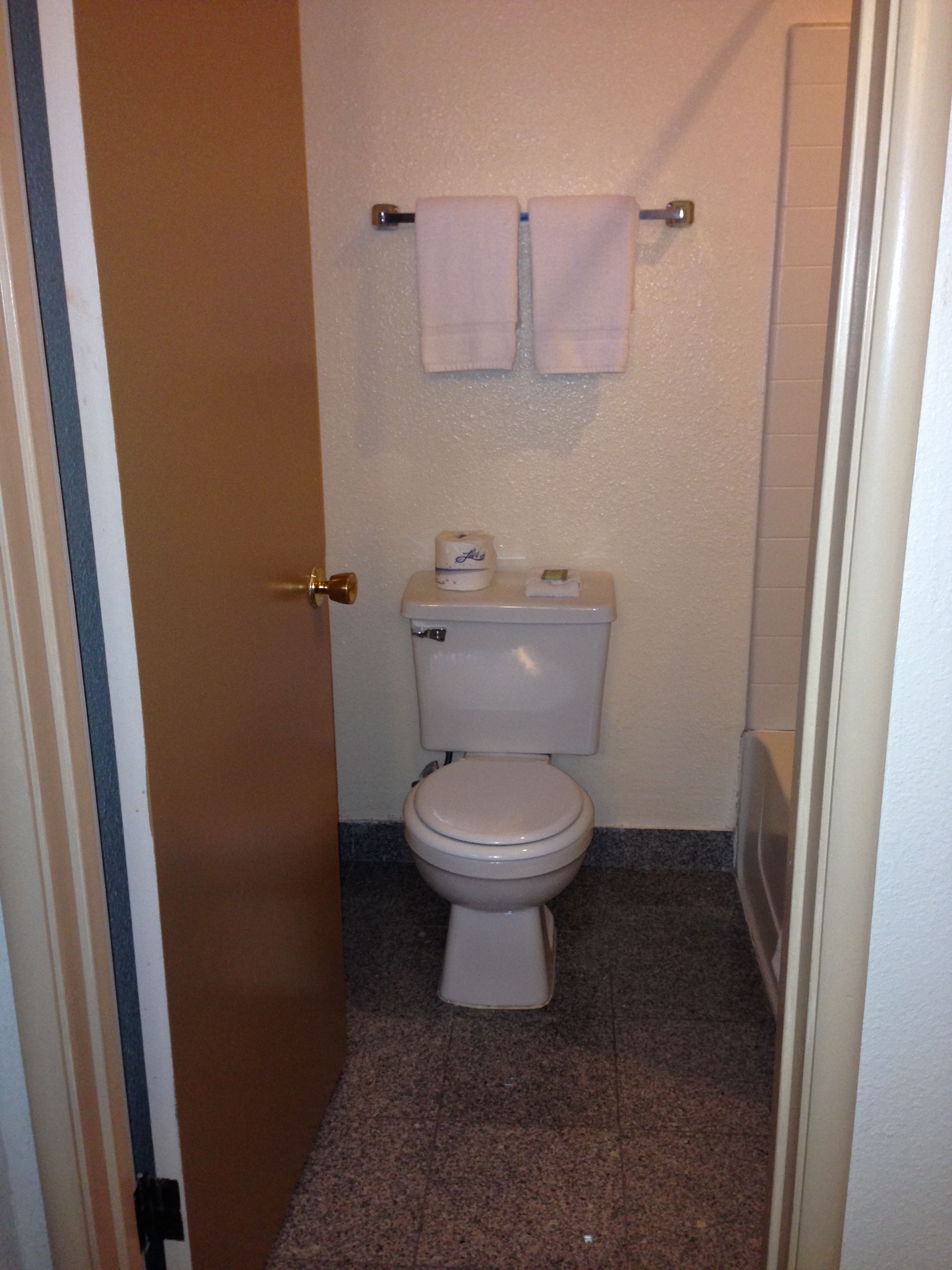 A small bathroom with a toilet, a towel rack with two towels, and a roll of toilet paper on the tank.