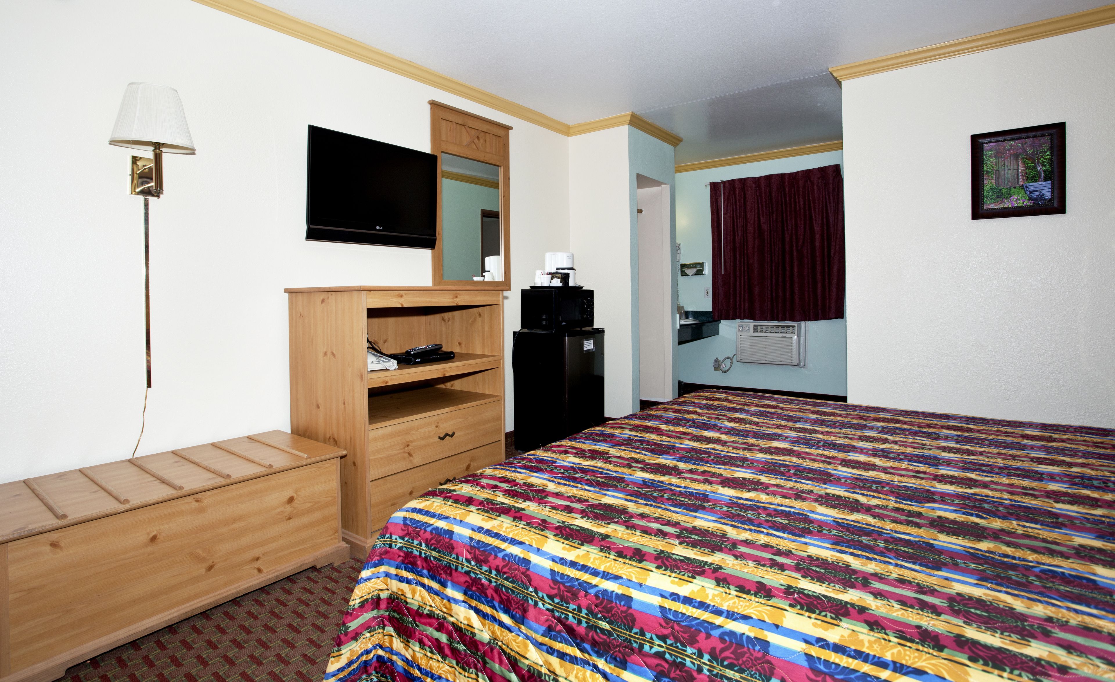 A hotel room with a wooden dresser, a bed with a colorful quilt, a television, a microwave, and a small kitchenette.