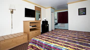 A hotel room with a wooden dresser, a bed with a colorful quilt, a television, a microwave, and a small kitchenette.