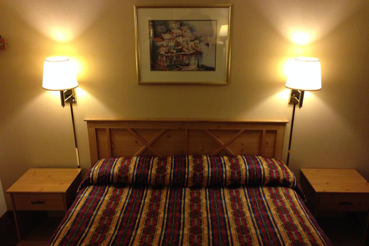 A bed with a striped bedspread, two bedside lamps, a framed picture on the wall, and wooden headboard and nightstands.