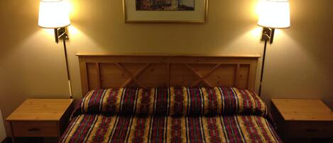 A bed with a striped bedspread, two bedside lamps, a framed picture on the wall, and wooden headboard and nightstands.