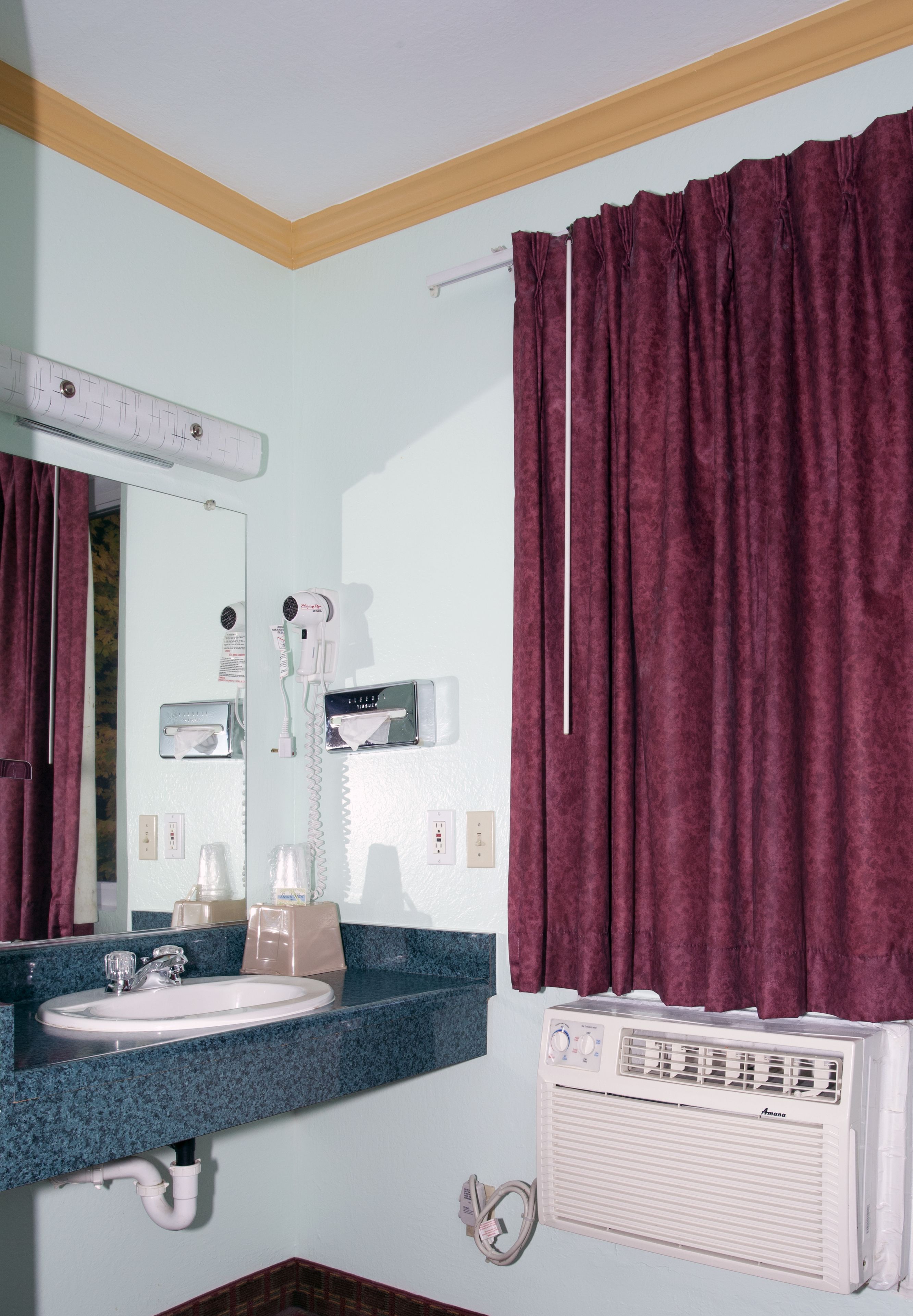 A bathroom with a sink, mirror, hairdryer, and a wall-mounted heater.