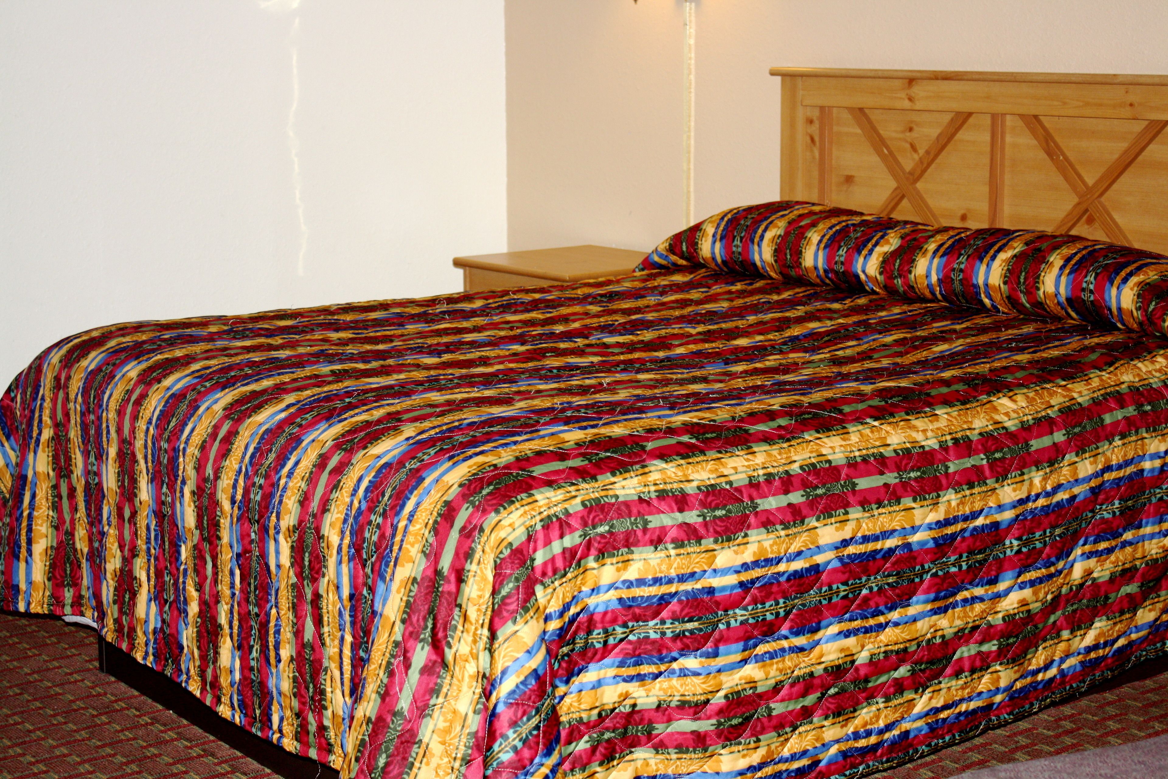 Een bed met een kleurrijke quilt, een houten hoofdbord en een nachtkastje.