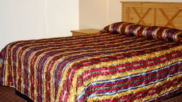 Een bed met een kleurrijke quilt, een houten hoofdbord en een nachtkastje.