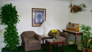 Una habitación con dos sillones, una mesita con un jarrón de girasoles, una lámpara y una estantería.
