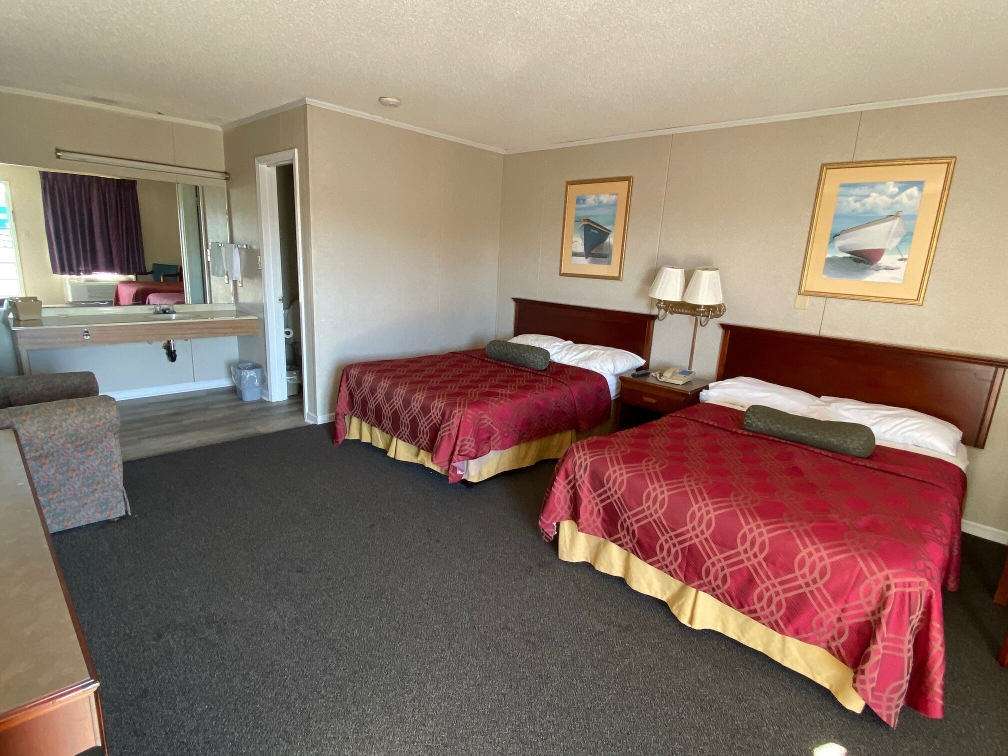 Habitación de hotel con dos camas, baño y un pequeño rincón de descanso.