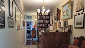 A cozy hallway with a wooden floor, a red sofa, a bookshelf, and various framed pictures on the walls. - The Scotsman Inn (Pictou)