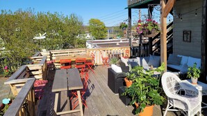An outdoor patio with wooden tables and chairs, potted plants, and a wooden deck. - The Scotsman Inn (Pictou)