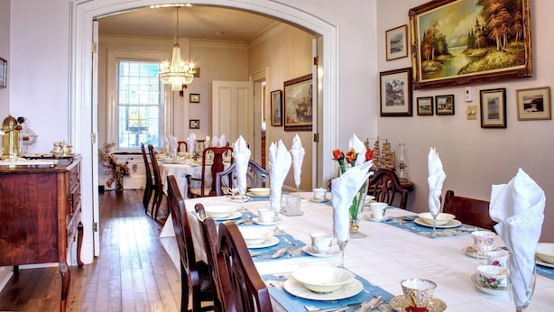 A dining room with a long table set for a meal, framed artwork on the walls, and a chandelier. - The Scotsman Inn (Pictou)
