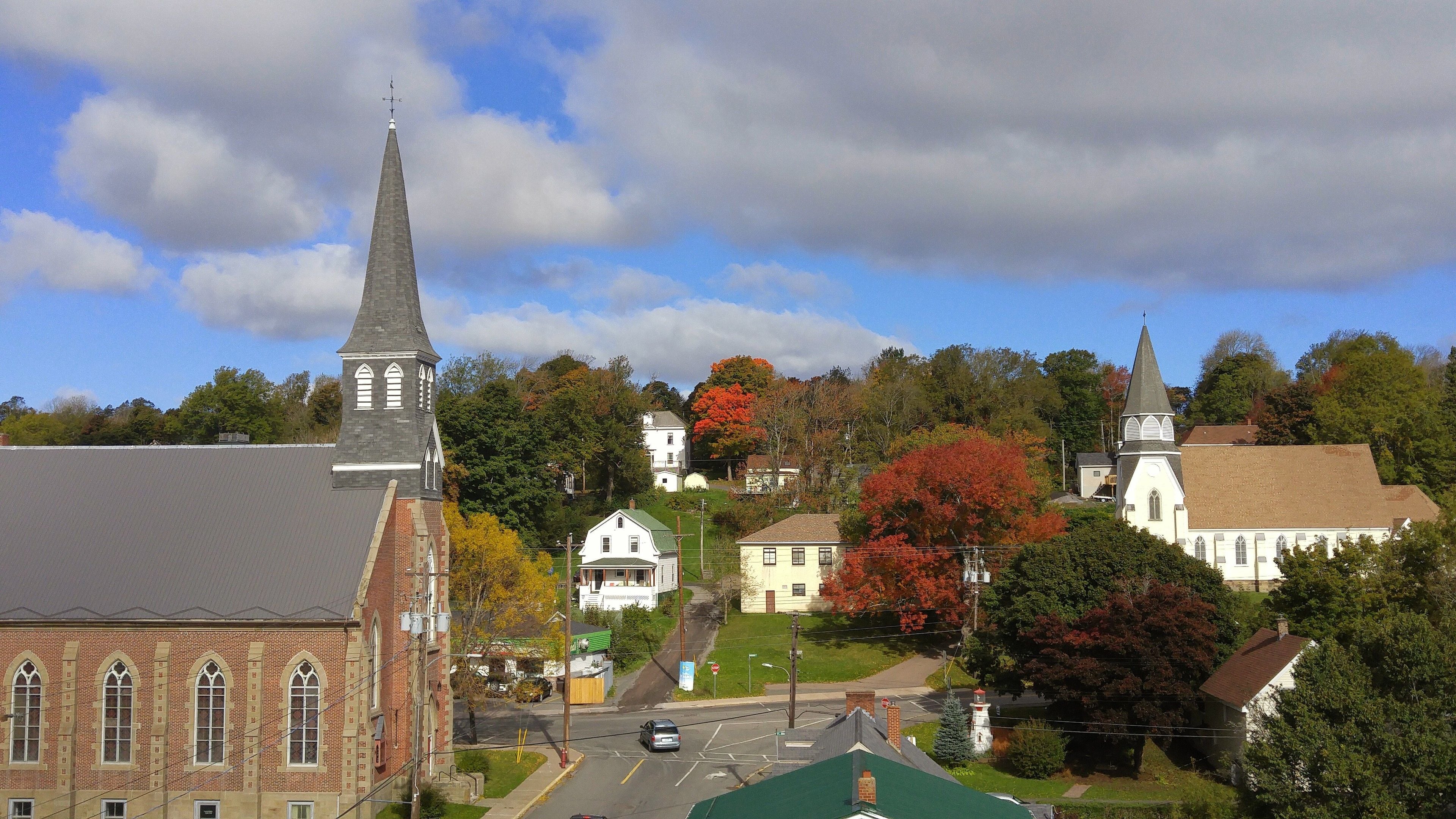 A town with a prominent church steeple, a brick building with arched windows, and a mix of residential houses.