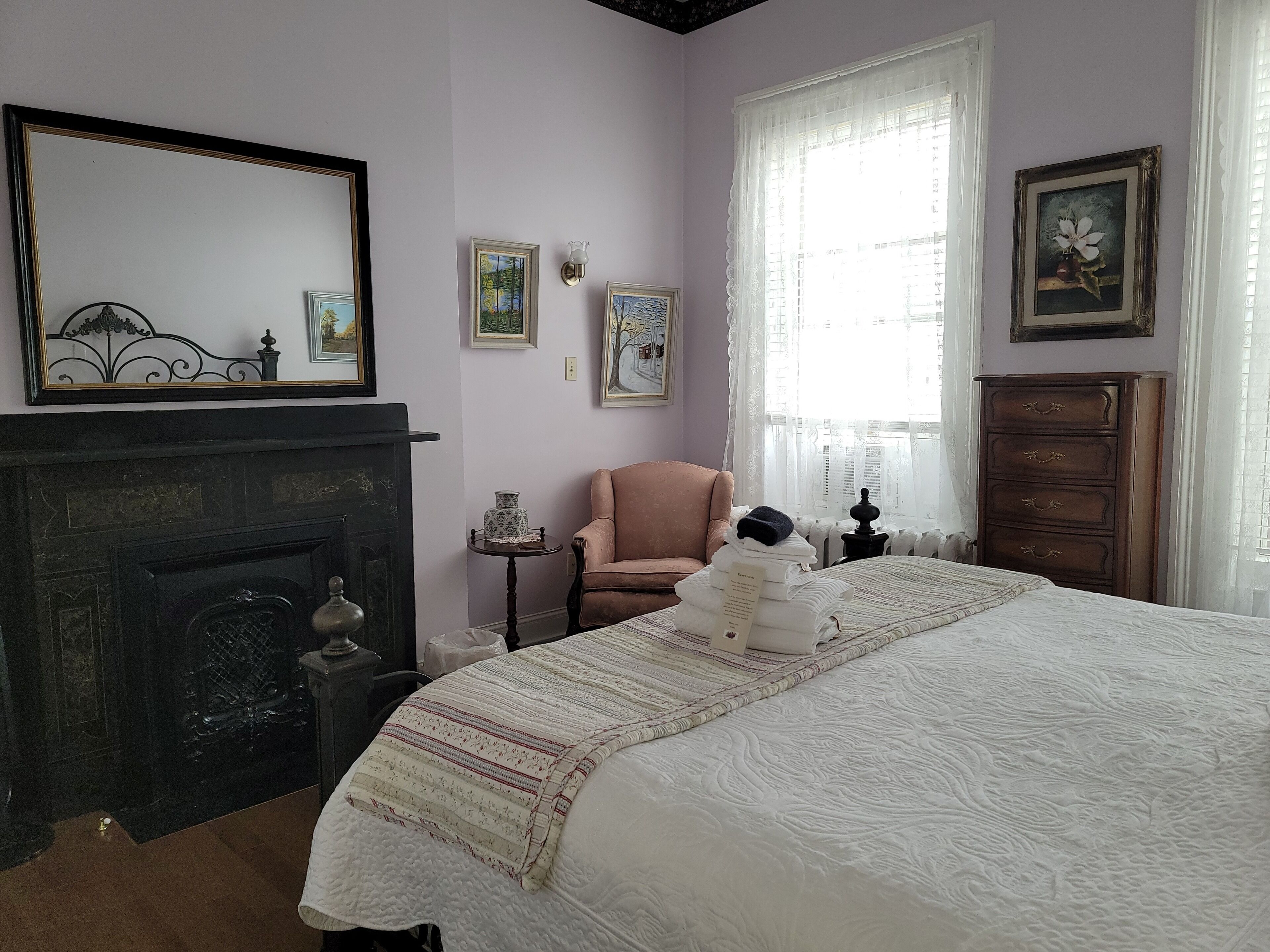 A bedroom with a large bed, a fireplace, a chair, and a dresser.