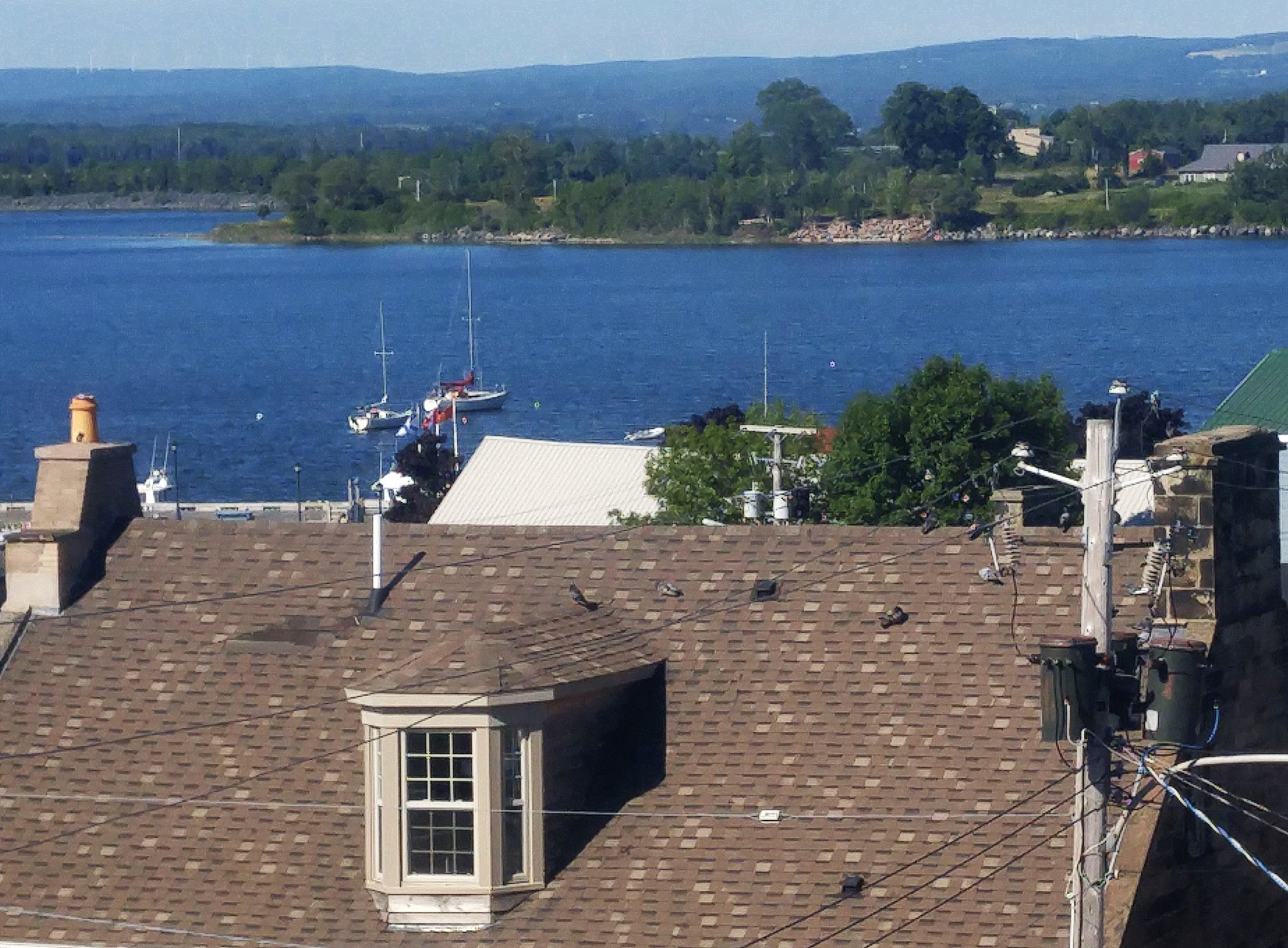 A view of a waterfront property with a brick roof, a small windowed structure, and a view of boats on the water.