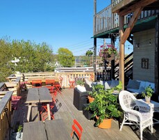 An outdoor patio with wooden tables and chairs, potted plants, and a view of the surrounding area.