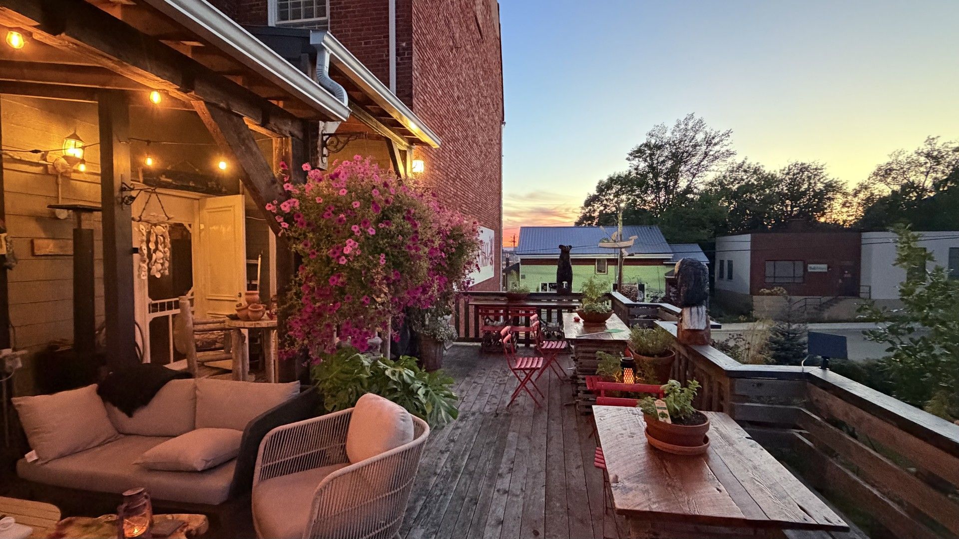 An outdoor patio area with wooden furniture, potted plants, and a view of a building in the background.