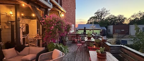 Un espacio de patio al aire libre con muebles de madera, plantas en macetas y vista de un edificio al fondo.