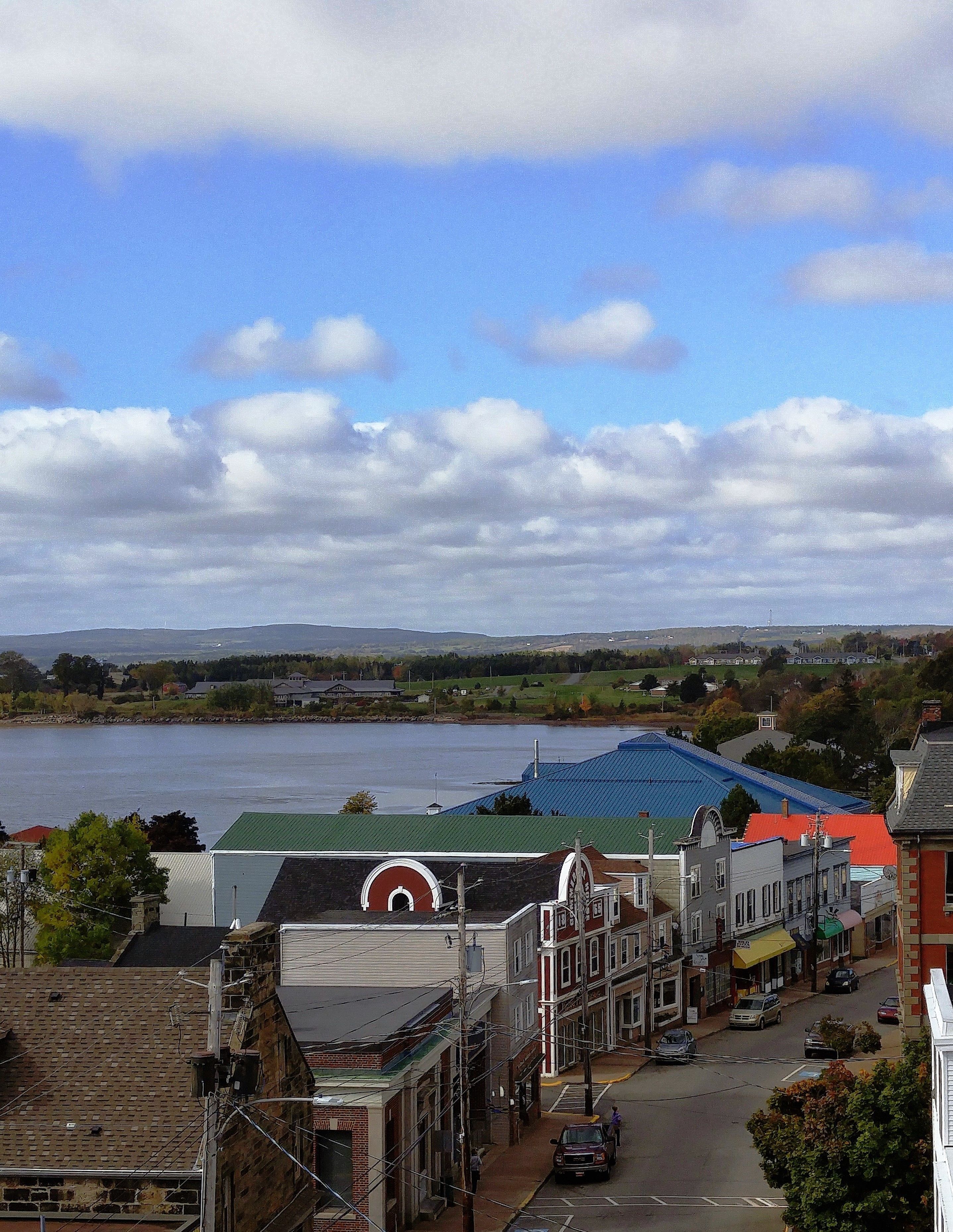 Un pueblo a orillas del río, con edificios a lo largo de la orilla, cielo despejado y vistas lejanas de colinas.